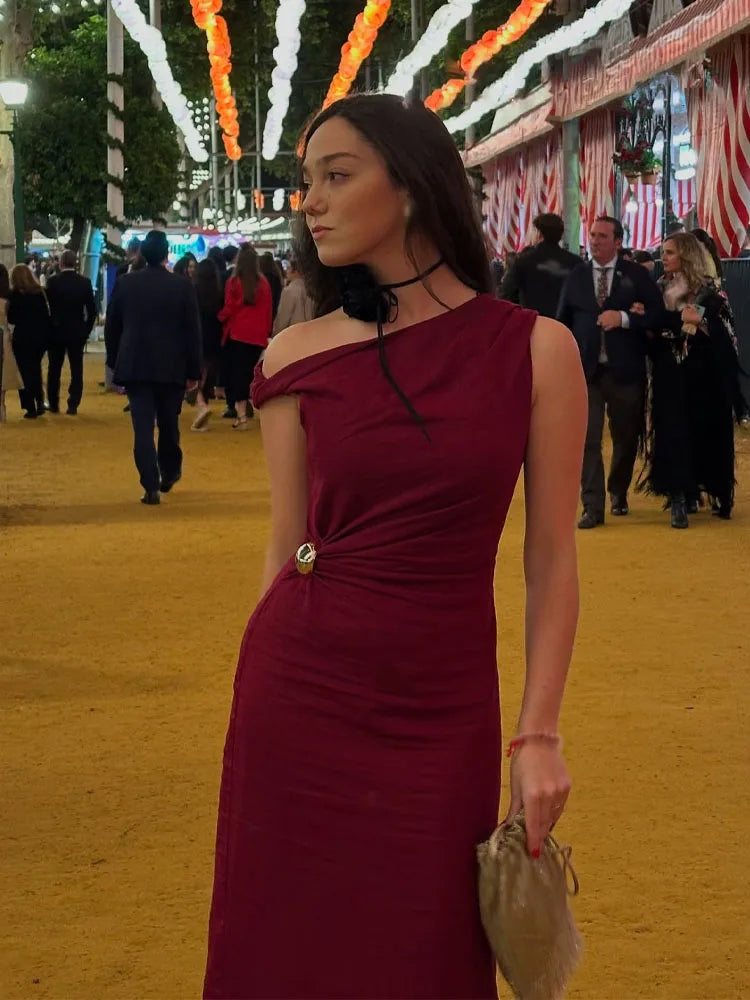Woman in a burgundy dress standing in an outdoor setting with people and decorations.