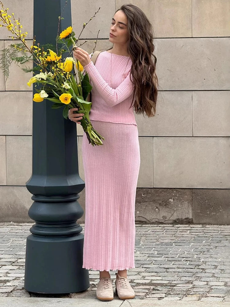 Woman in a pink outfit holding flowers against a stone wall.