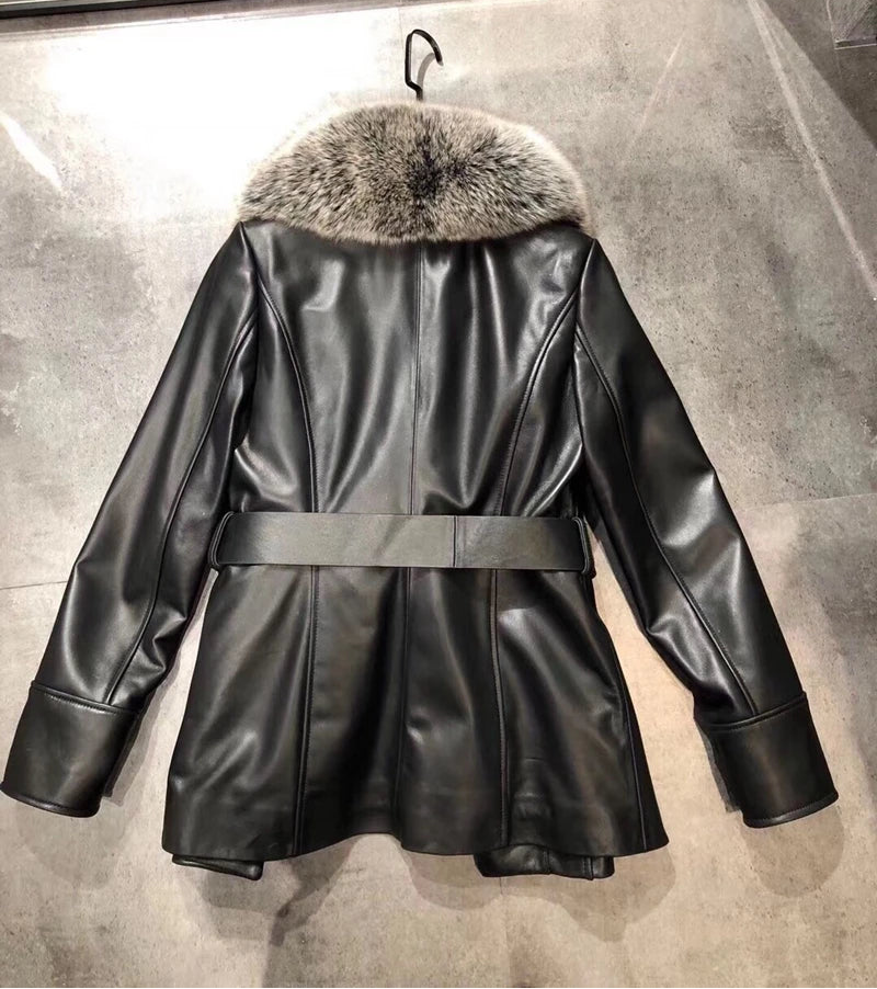 Black leather coat with fur collar on a hanger against a gray concrete wall.