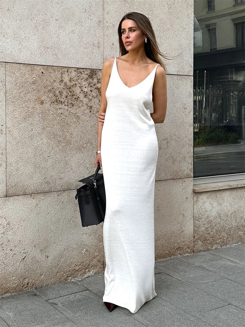 Woman in a white slip dress standing against a textured wall.