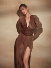 Woman wearing a brown evening gown with a deep neckline and slit on a beige background