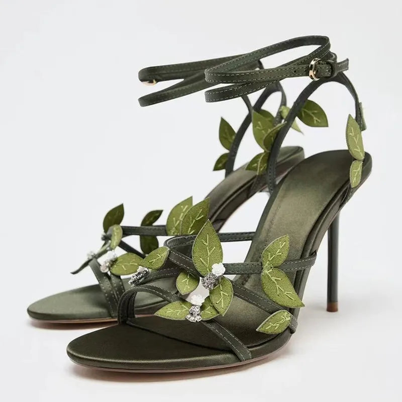 Green high-heeled sandals with leaf designs on a white background