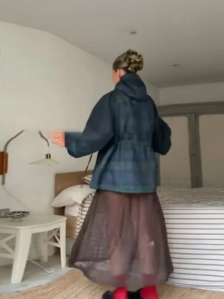 Person wearing a blue coat and brown skirt in a bedroom setting