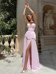 Woman in a pink evening gown with a high slit standing in an outdoor setting with classical architecture.