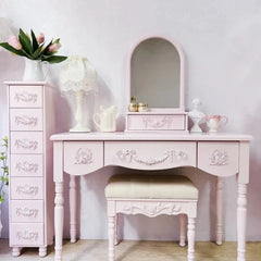 Pink vanity table with mirror, drawers, and stool in a room setting.