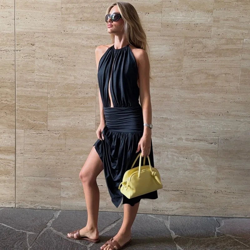 Woman in a black dress holding a yellow handbag against a beige wall.