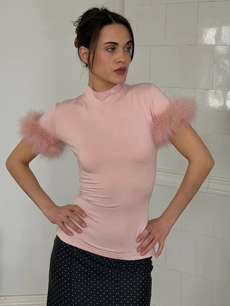 Woman wearing a pink top with fluffy sleeves against a tiled wall.
