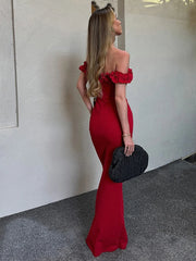 Woman in a red off-shoulder dress holding a black clutch against a neutral wall.