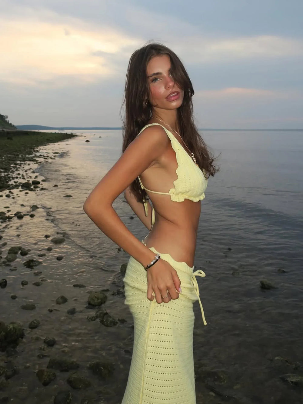 Woman in a yellow bikini standing on a beach with water and sky in the background