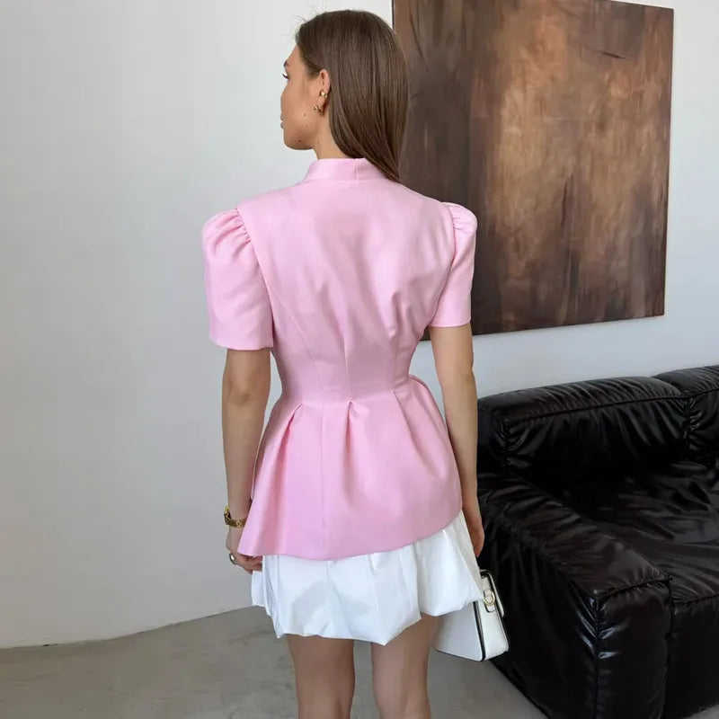 Woman wearing a pink top and white skirt standing in a room with a black sofa and wooden wall art.