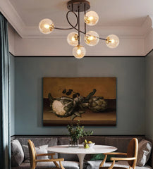 Modern chandelier hanging above a dining table with a still life painting on the wall.