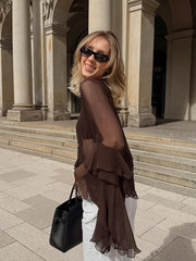 Woman in a sheer brown dress standing in front of classical architecture.