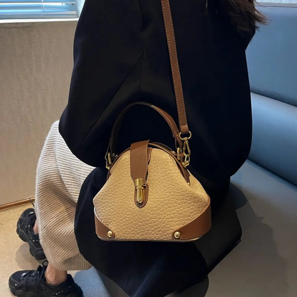 Woman wearing a black jacket and carrying a beige and brown textured dome satchel bag.