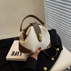 Close-up of a white and brown textured dome satchel bag with contrast trim and gold hardware.