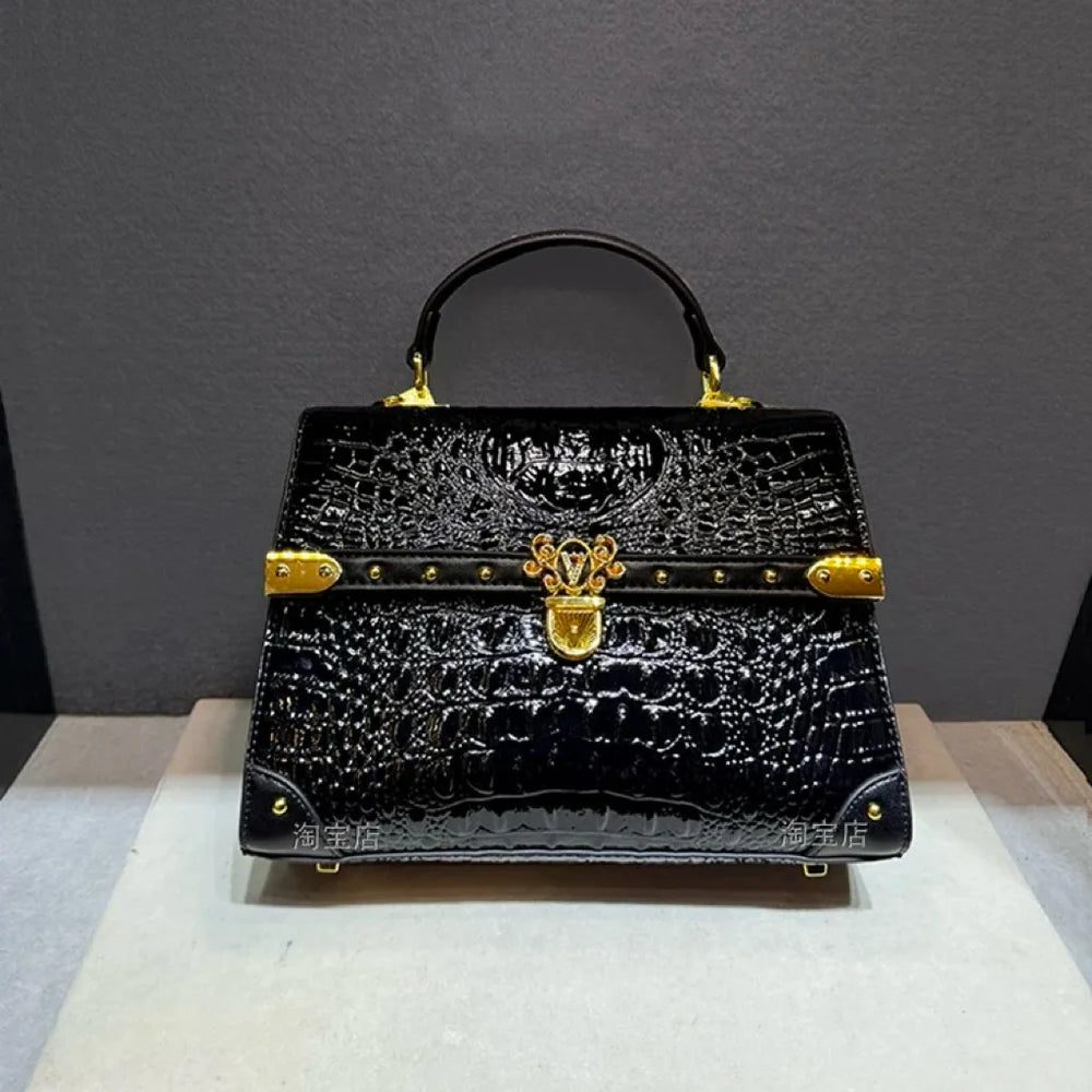 Structured crocodile embossed leather top handle bag in black with gold hardware, side view.