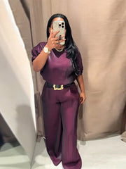 Person wearing a purple outfit with a belt, standing against a neutral background.