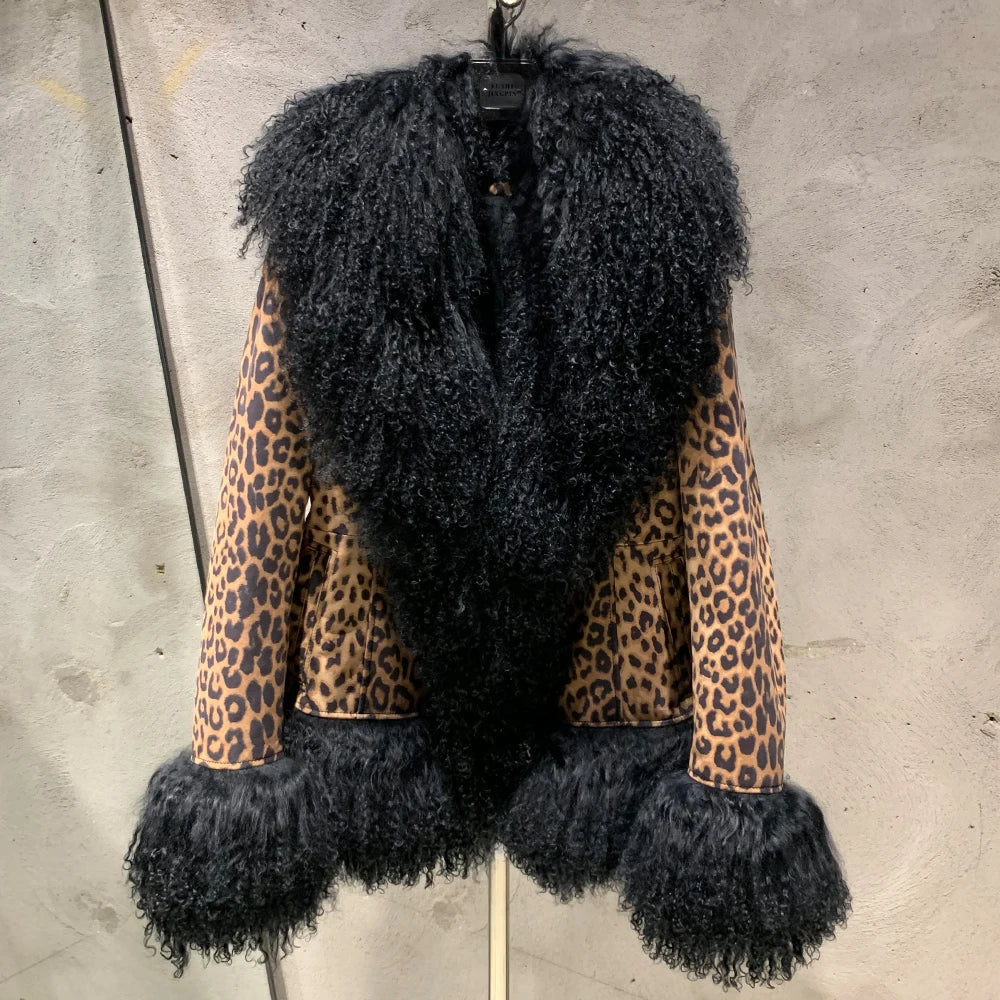 Black fur vest with leopard print sleeves on a hanger against a concrete wall.