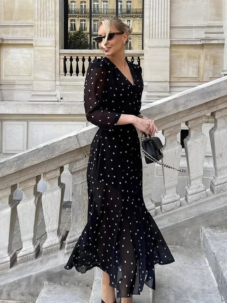 Woman in a black polka dot dress standing on a stone staircase with classical architecture.