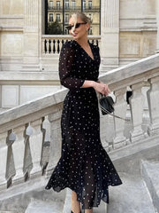 Woman in a black polka dot dress standing on a stone staircase with classical architecture.