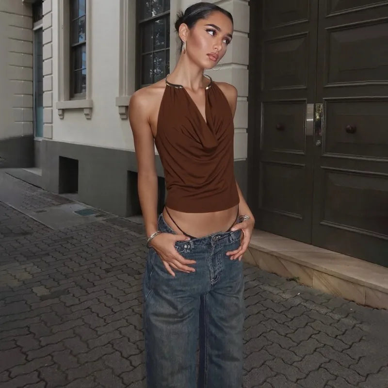 Woman in a brown top and blue jeans standing on a street.