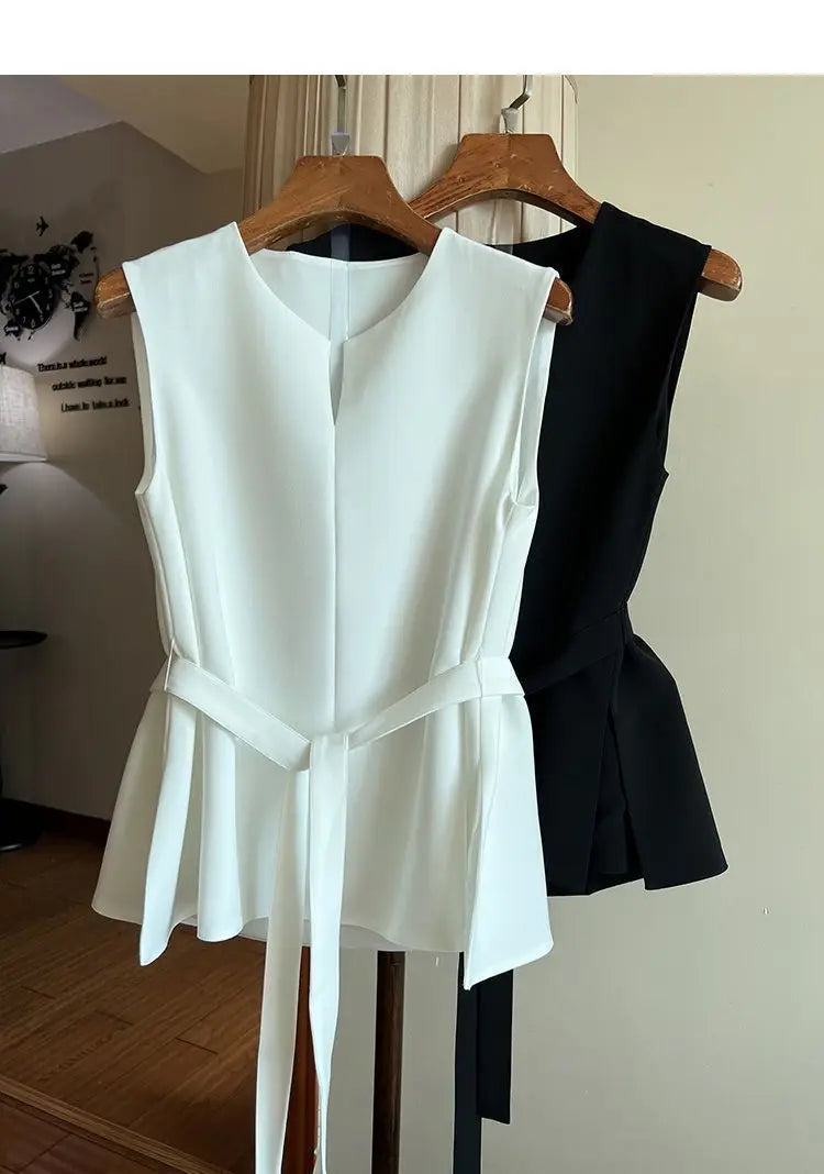 White and black sleeveless tops hanging on wooden hangers against a neutral wall.