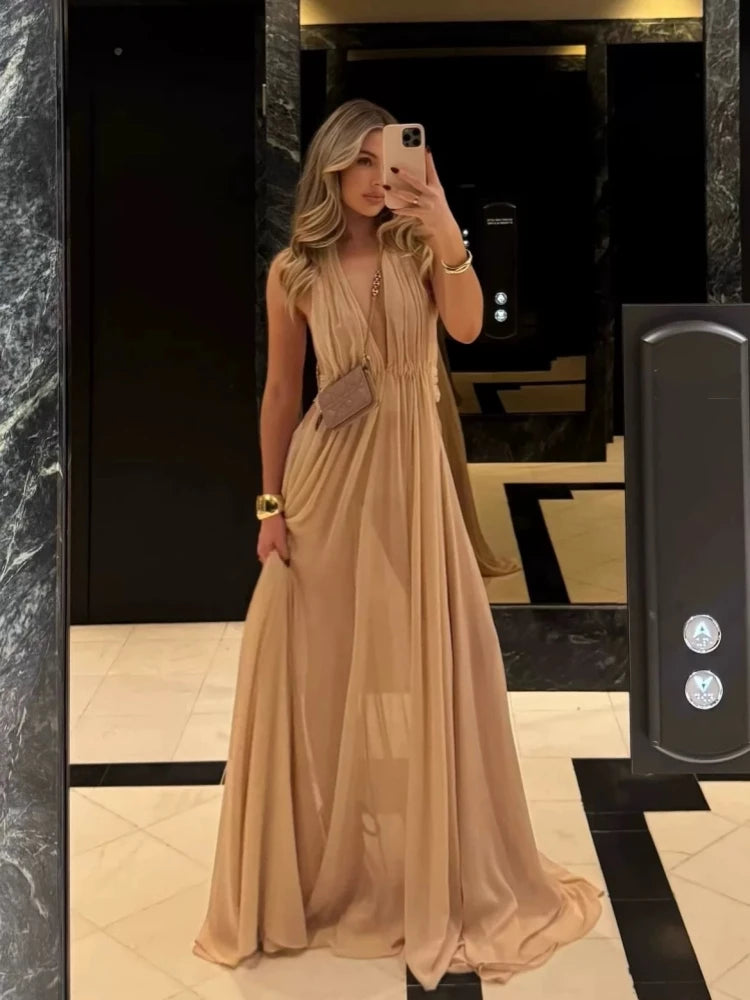Woman in a beige dress taking a mirror selfie in an indoor setting.