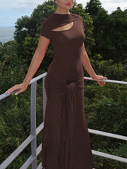Woman in a brown dress standing on a balcony with greenery and water in the background