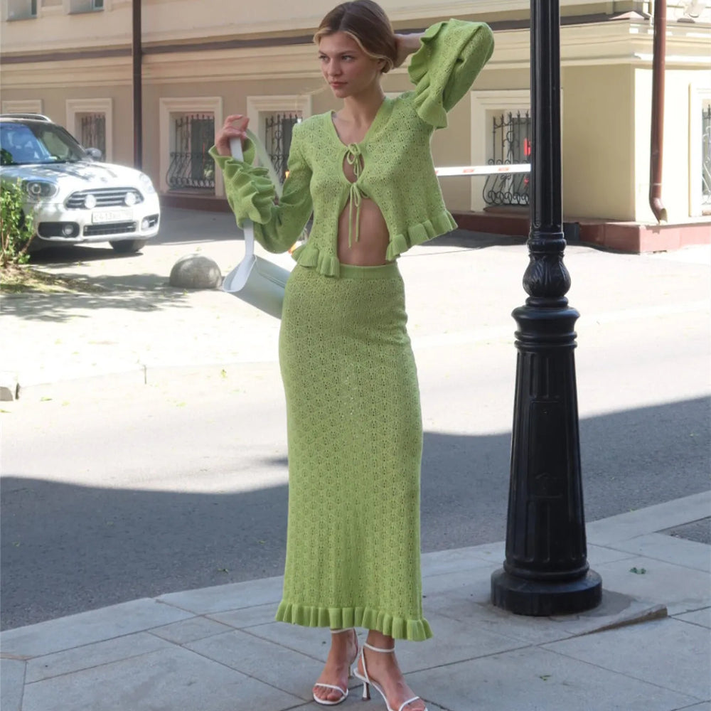 Woman in a green knit outfit standing on a street corner.