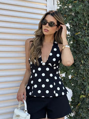 Woman wearing a black polka dot top and shorts, standing against a corrugated metal wall.