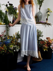 Woman wearing a light blue dress with lace details standing among flowers.