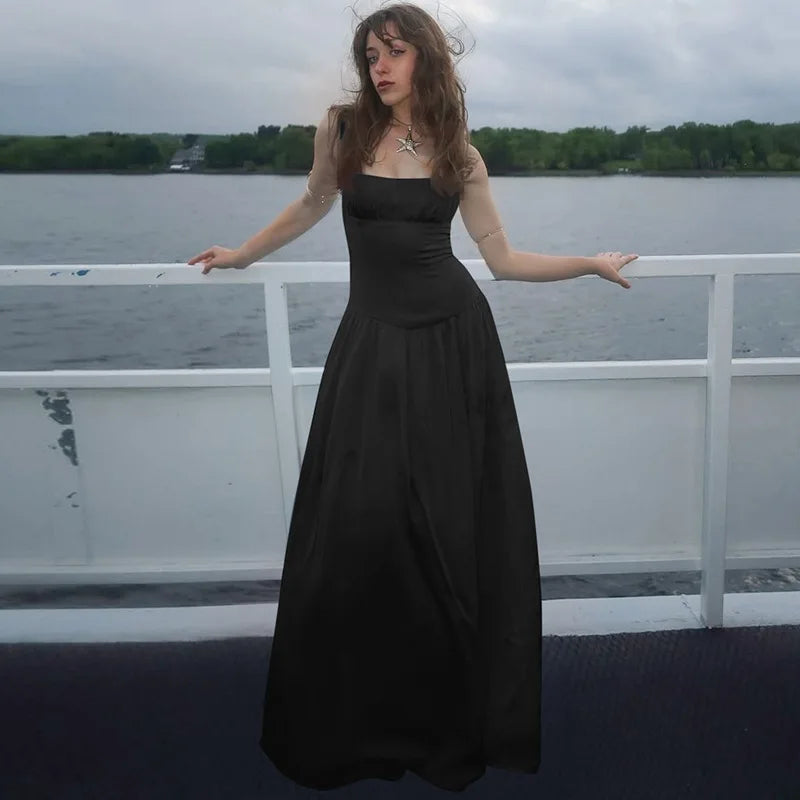 Woman in a black dress standing on a boat with water and trees in the background