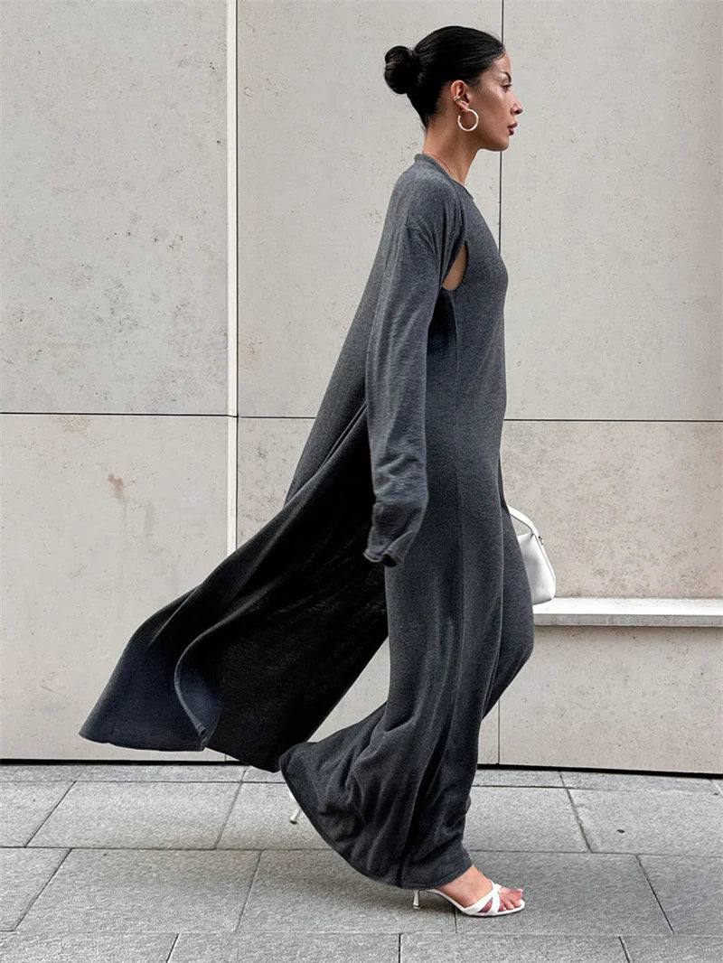 Woman wearing a long gray dress against a light-colored wall.
