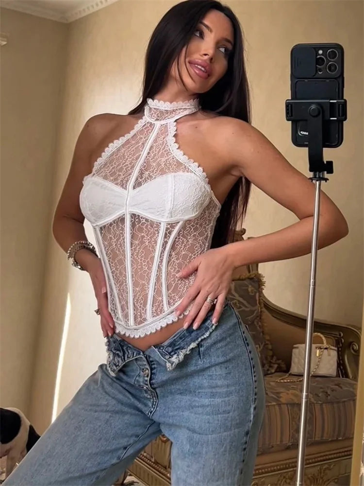 Woman wearing a white lace top and blue jeans in a room with a mirror and camera on a stand.
