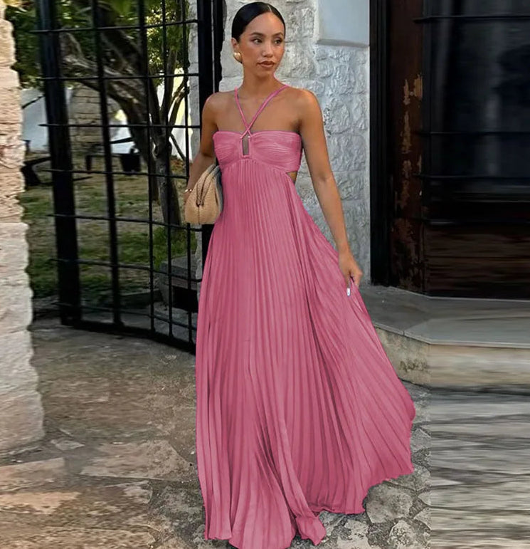 Woman in a pink pleated dress standing outdoors near a stone wall.