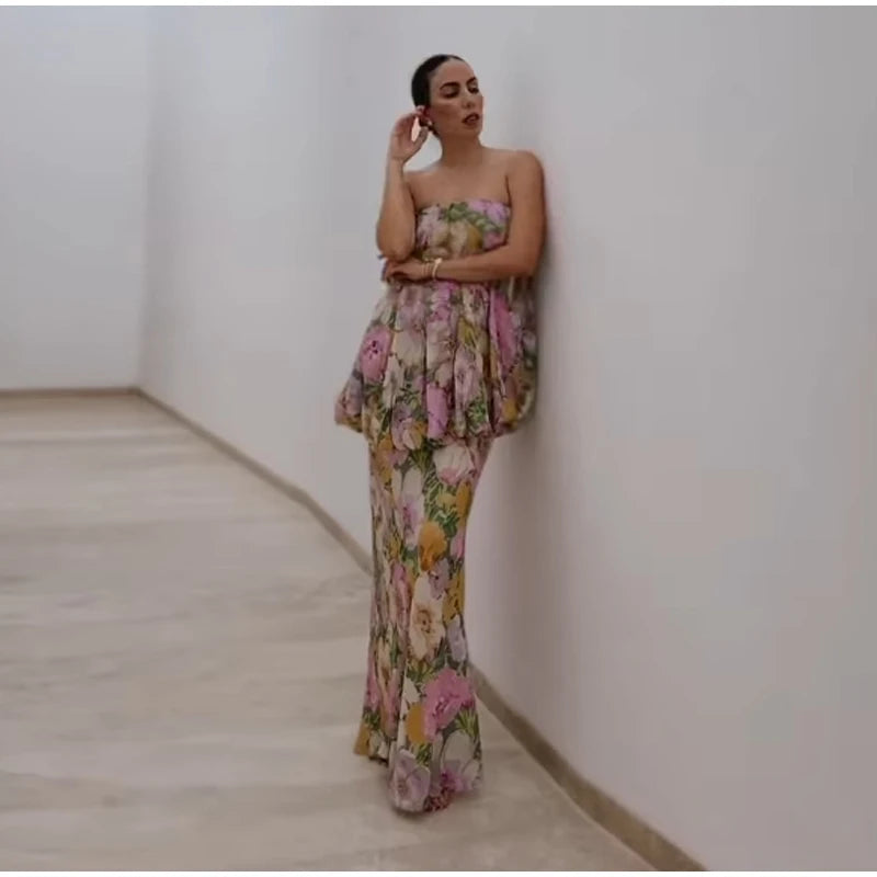 A woman wearing a floral strapless dress is standing against a white wall.