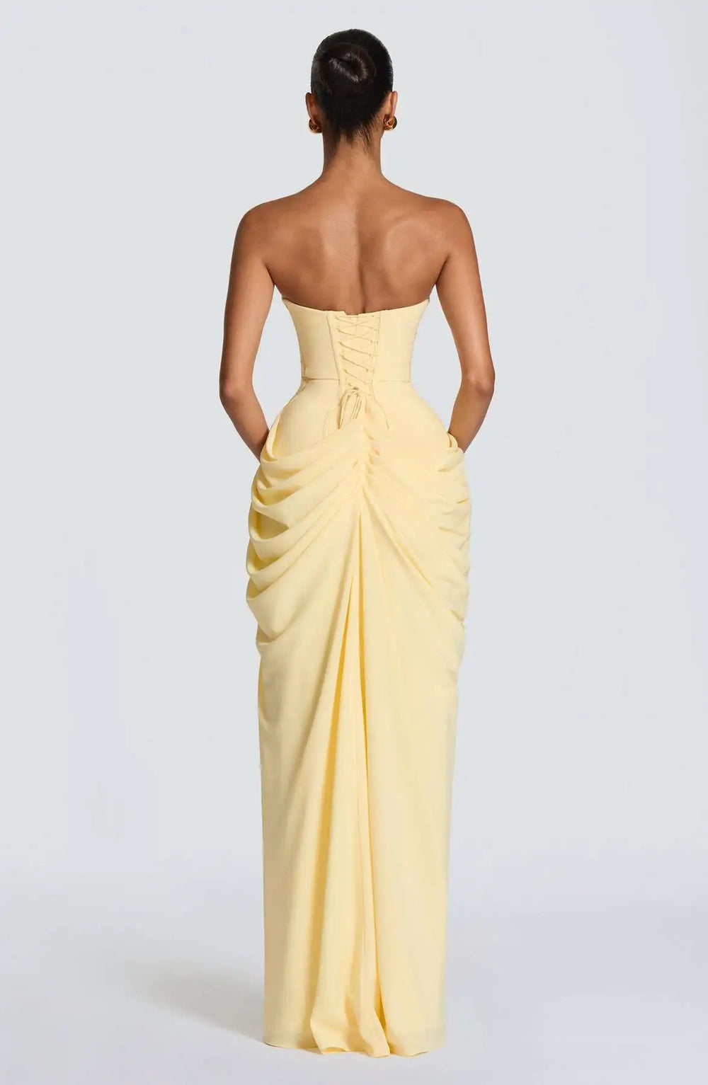Woman wearing a strapless yellow evening gown on a plain background