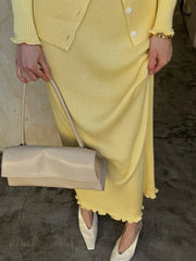 Person wearing a yellow outfit holding a beige handbag on a textured surface