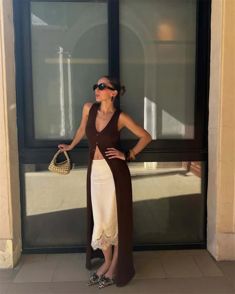 Woman in a long brown and white dress standing in front of a large window.