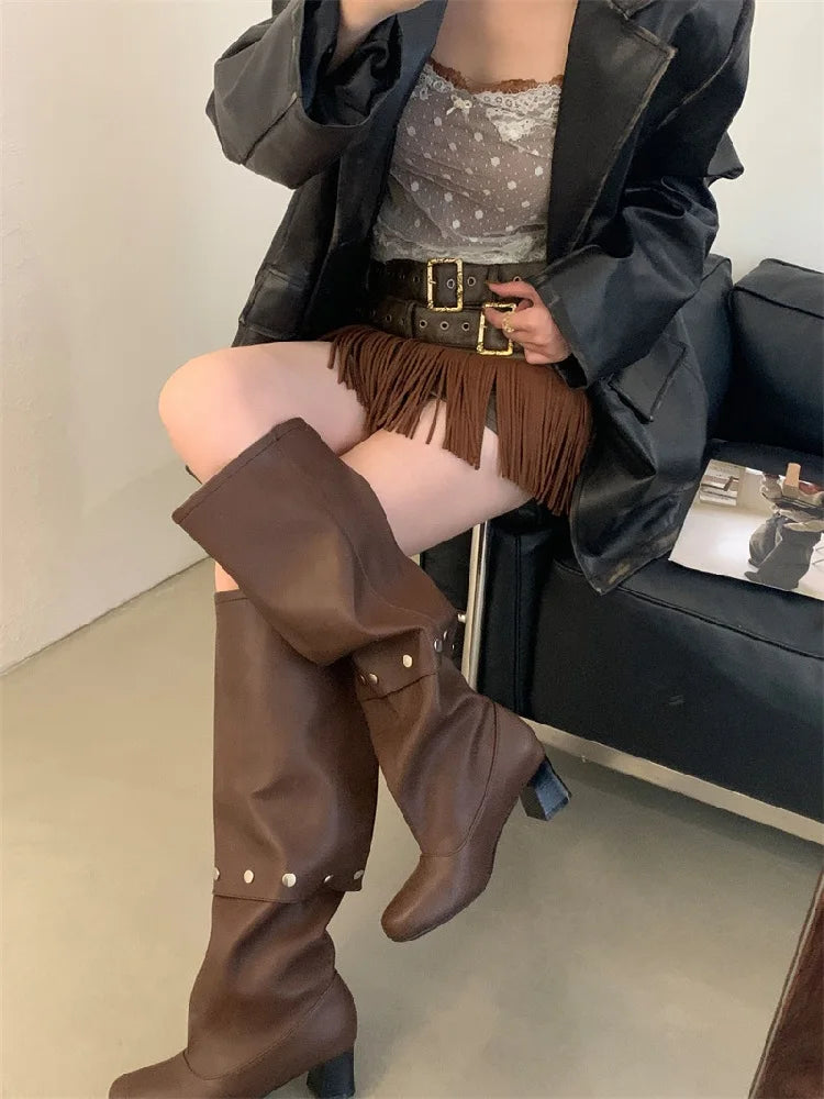 Person wearing brown knee-high boots sitting on a couch.