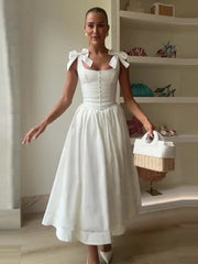 Woman in a white dress with bow straps holding a basket indoors.