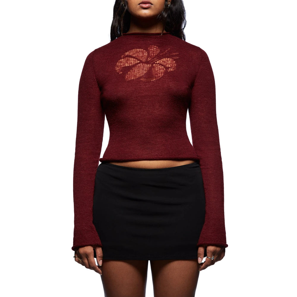 Person wearing a maroon long-sleeve top with a floral design and a black skirt