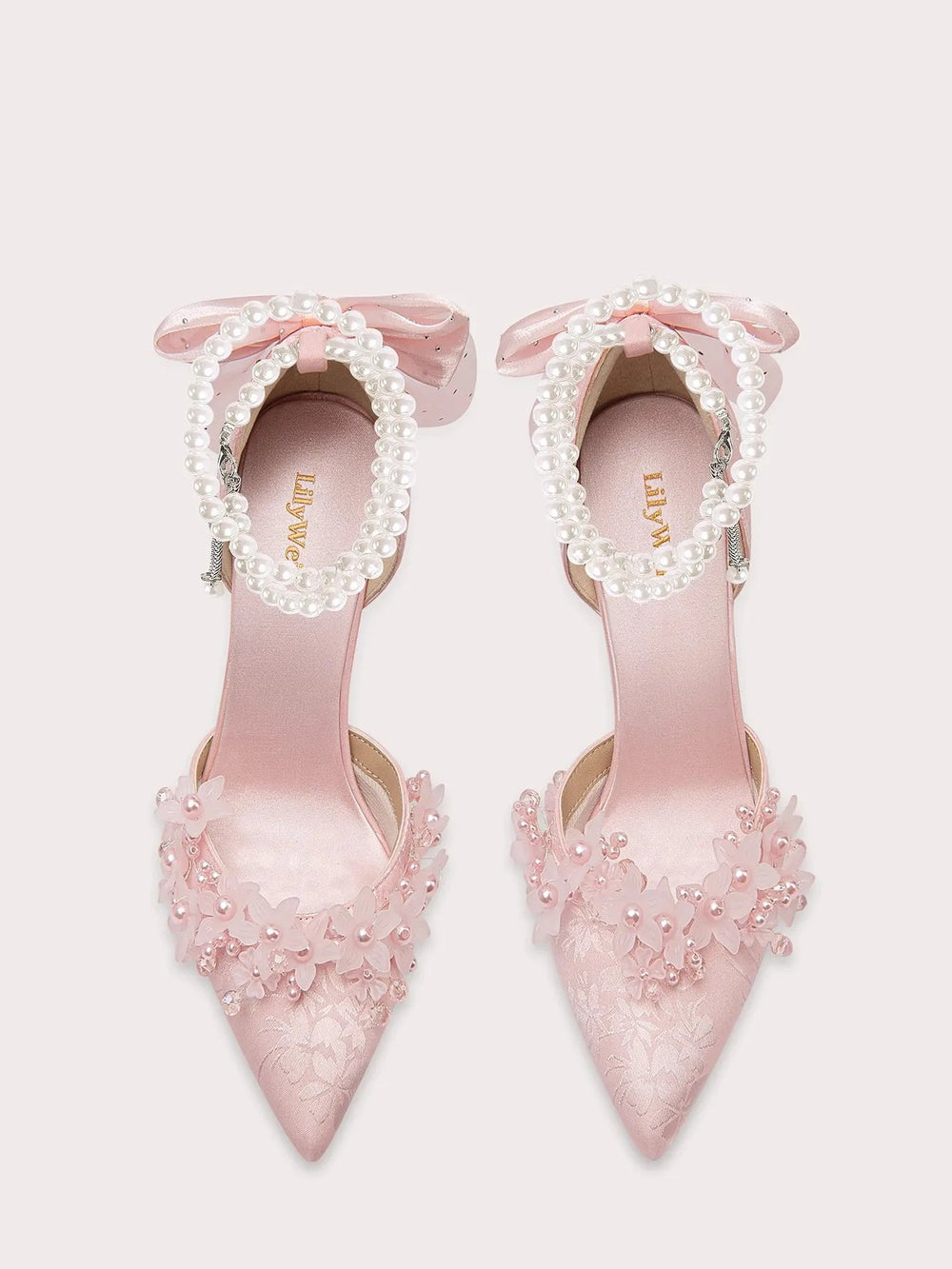 Pink high-heeled shoes with floral decorations and bow details on a white background