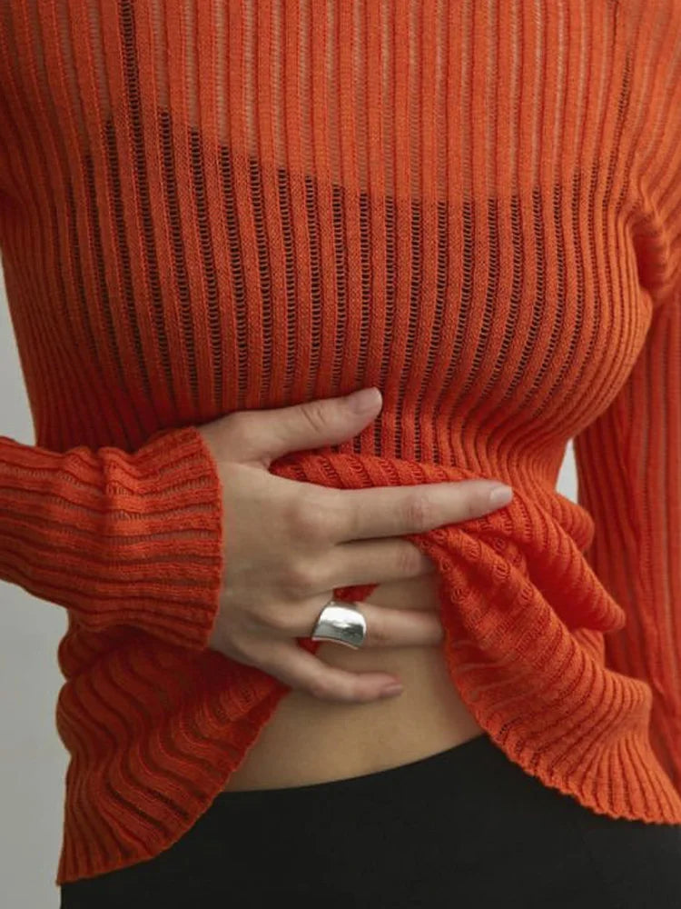 Person wearing an orange ribbed sweater with a hand adjusting the fabric against a neutral background