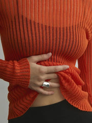 Person wearing an orange ribbed sweater with a hand adjusting the fabric against a neutral background