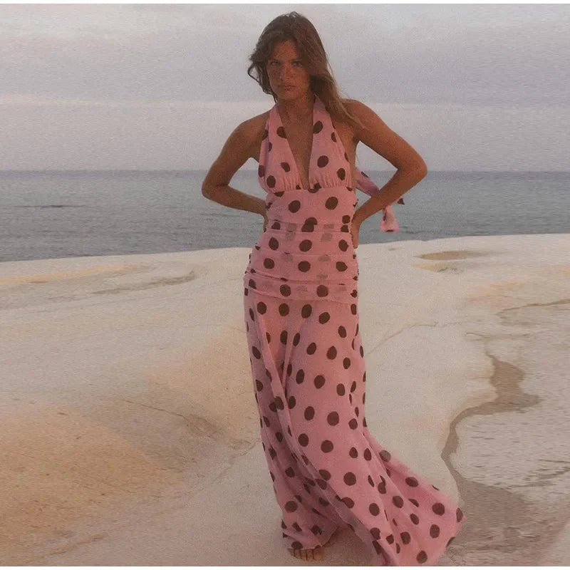 Woman in a pink polka dot dress standing on a rocky beach.