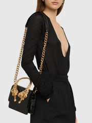 Woman wearing a black top and holding a black crocodile effect top handle bag with gold tiger sculptures