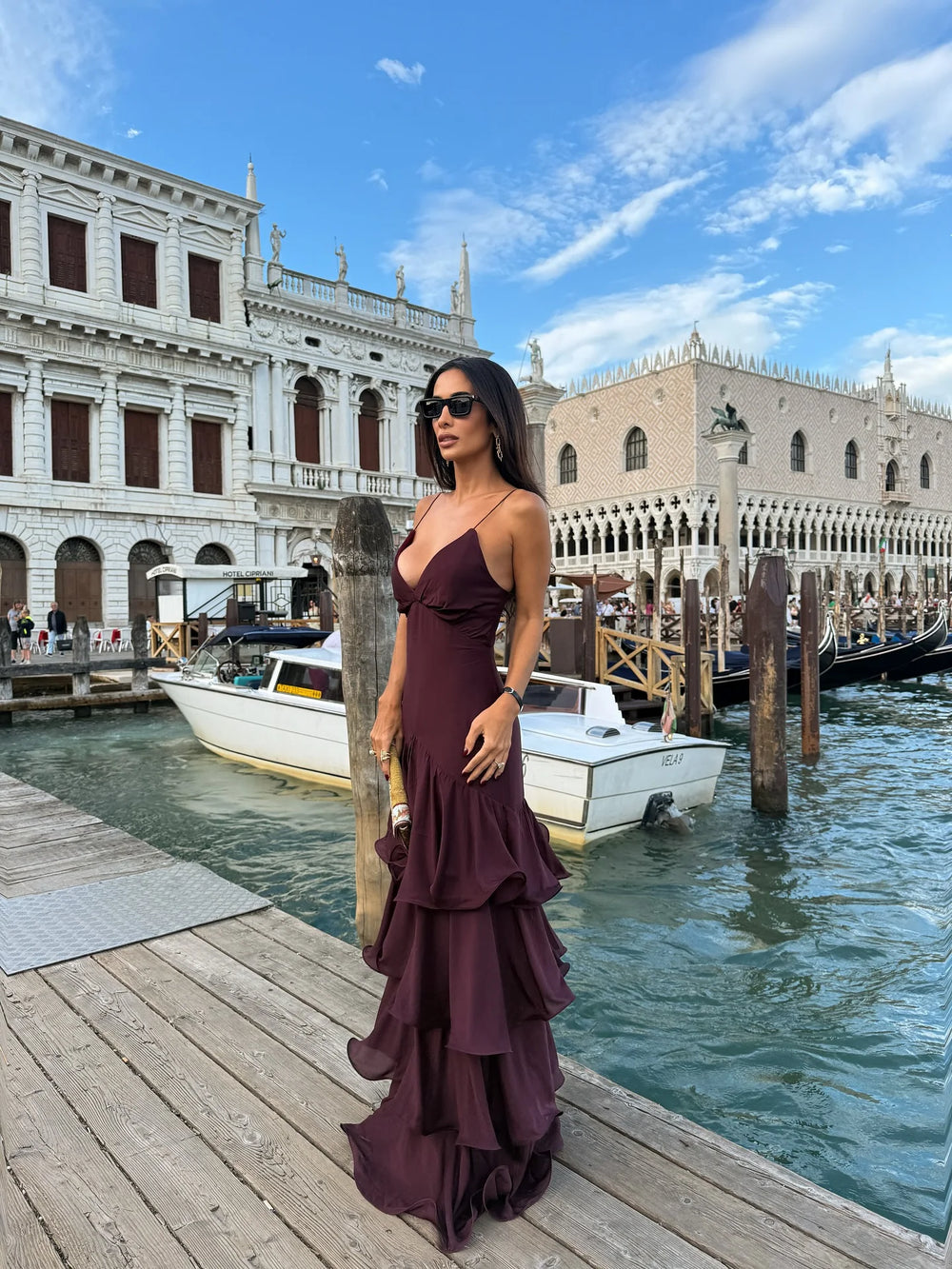 Woman in a purple dress standing on a dock with boats and historic buildings in the background