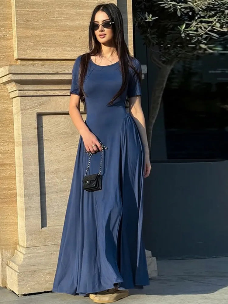 Woman in a blue dress standing outdoors near a building entrance.