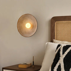 A round Japanese-style wall sconce with a warm glow, illuminating a cozy bedroom with minimalist decor. A