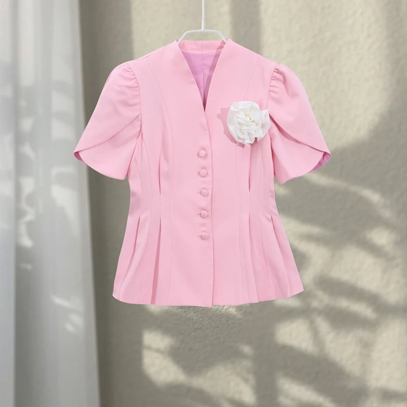 Pink blazer with a white flower accessory on a neutral background